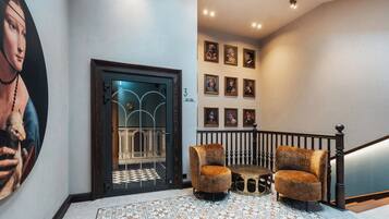 A hallway with a patterned floor, a large painting, a door with glass panels, and a staircase with a railing.