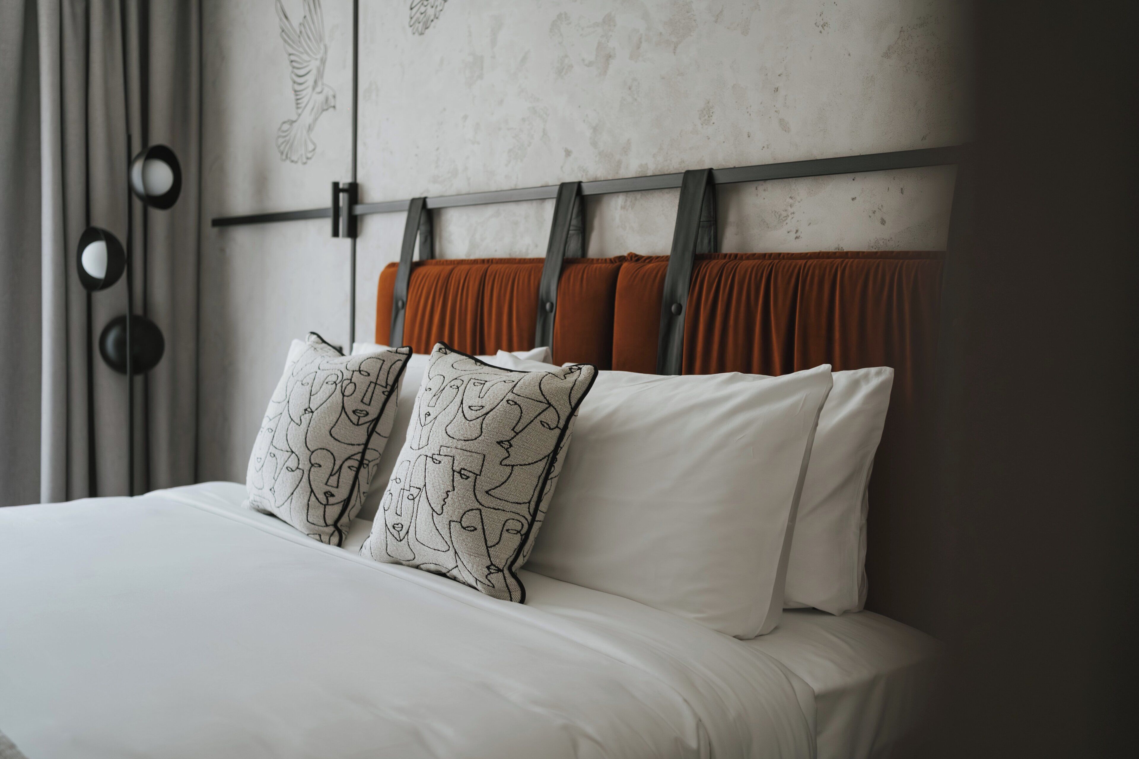 Una cama con sábanas blancas, cabecera de tela naranja y almohadas estampadas.
