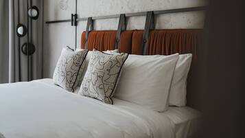 Una cama con sábanas blancas, cabecera de tela naranja y almohadas estampadas.