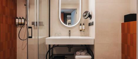 A modern bathroom with a glass-enclosed shower, a white sink with a mirror above, and a shelf with towels.