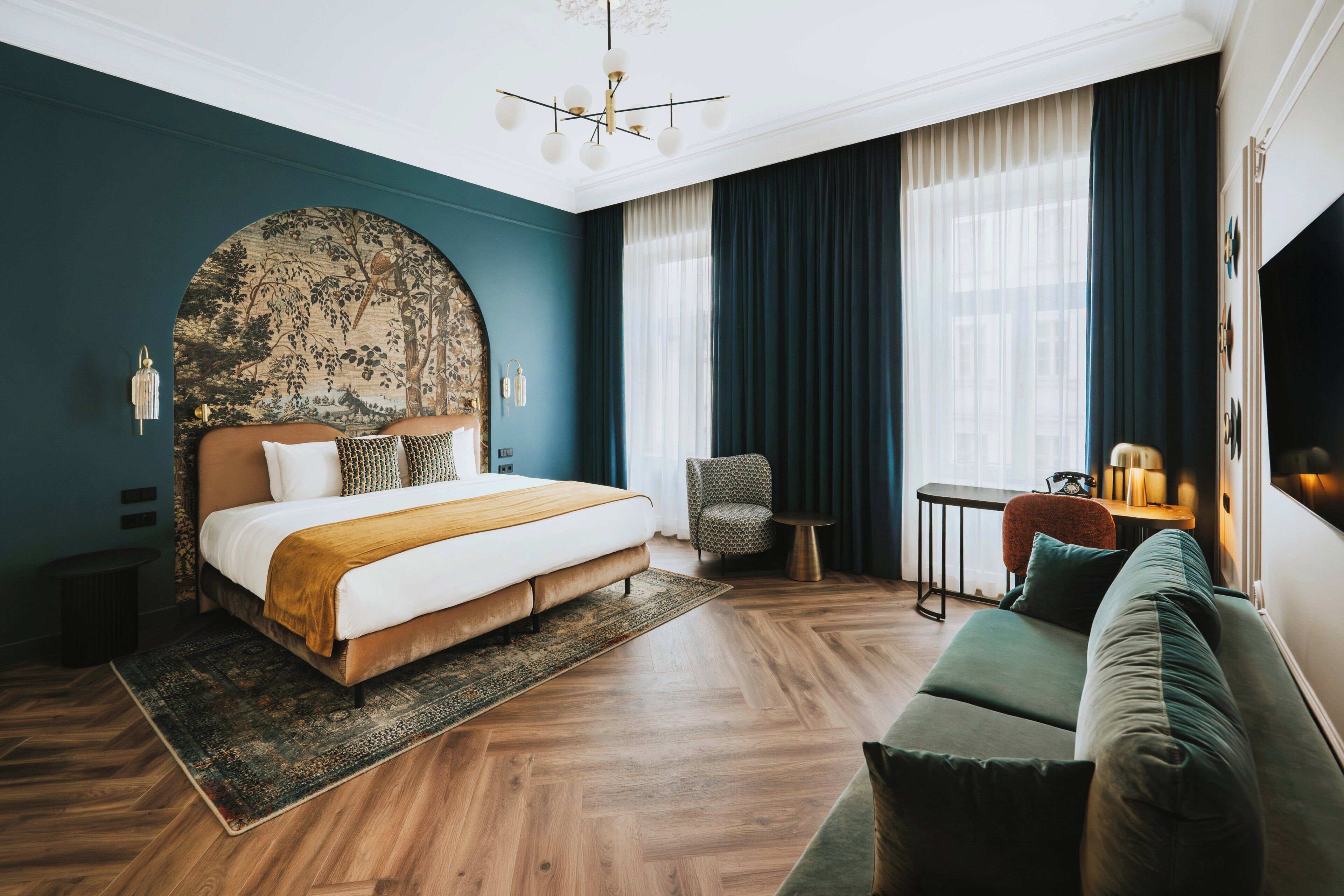 A bedroom with a large bed, a green sofa, a small table, and a chair.