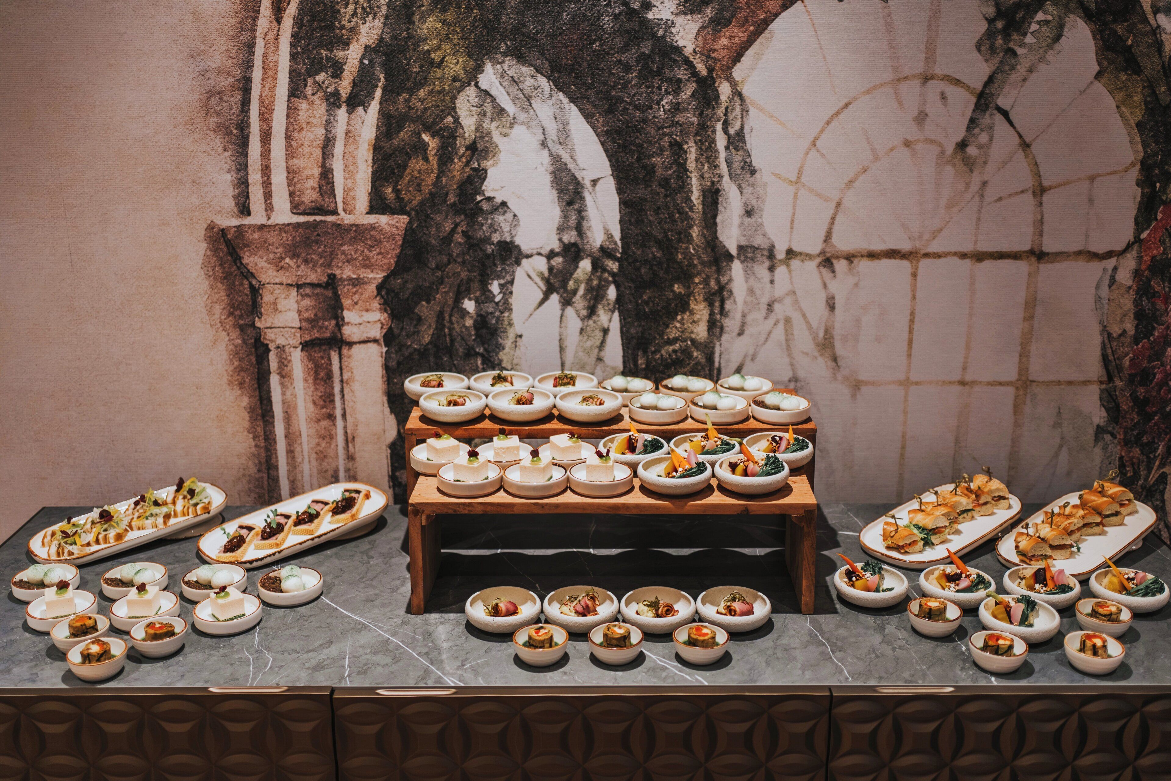 A buffet with various dishes arranged on a table against a wall with a decorative arch.