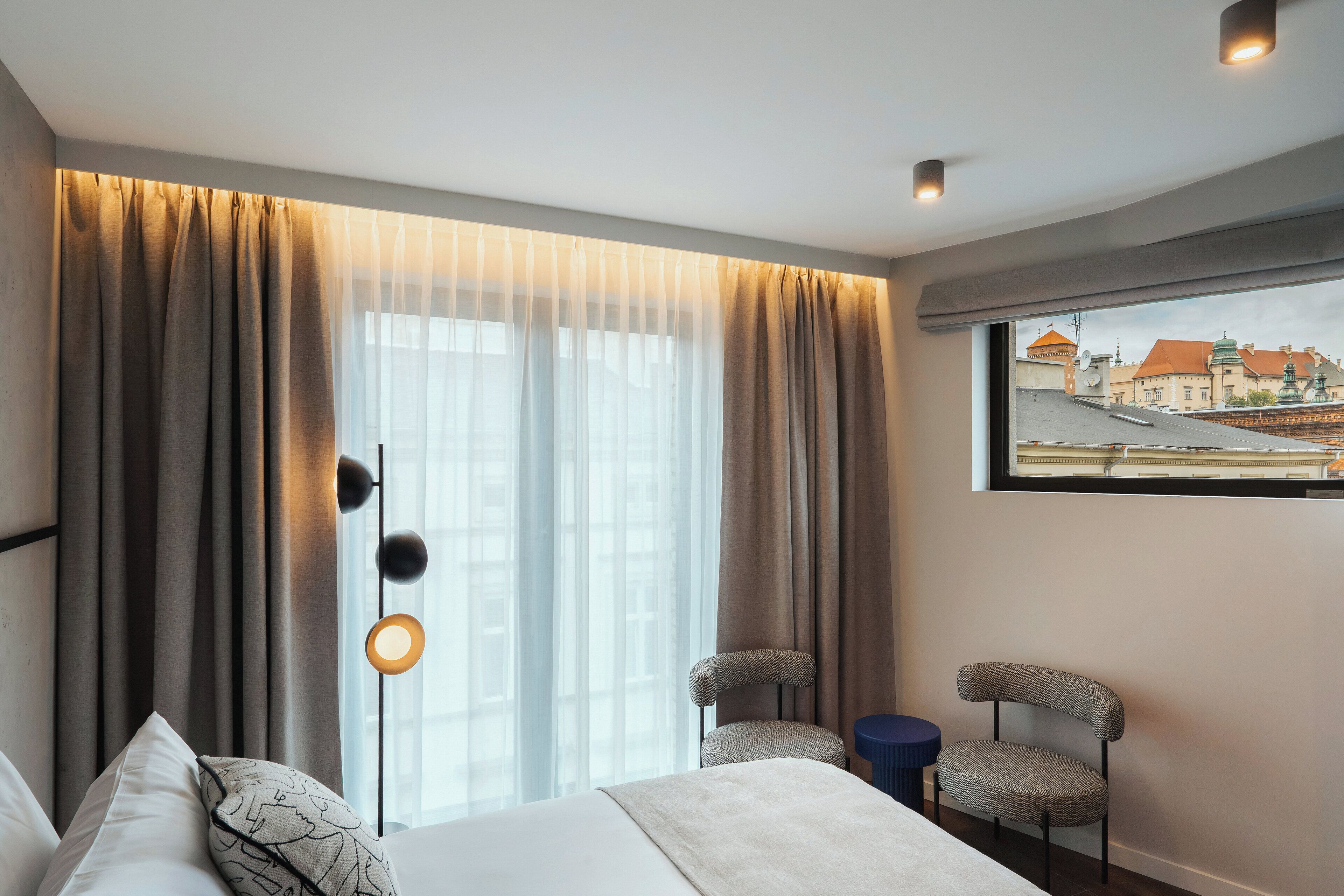 A hotel room with a large bed, two chairs, a small table, and a window with curtains.