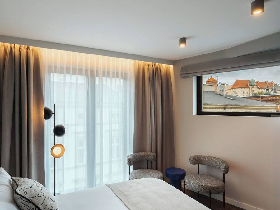 A hotel room with a large bed, two chairs, a small table, and a window with curtains.