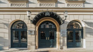 Fachada de hotel con una puerta azul oscuro, ventanas arqueadas y un toldo metálico decorativo.
