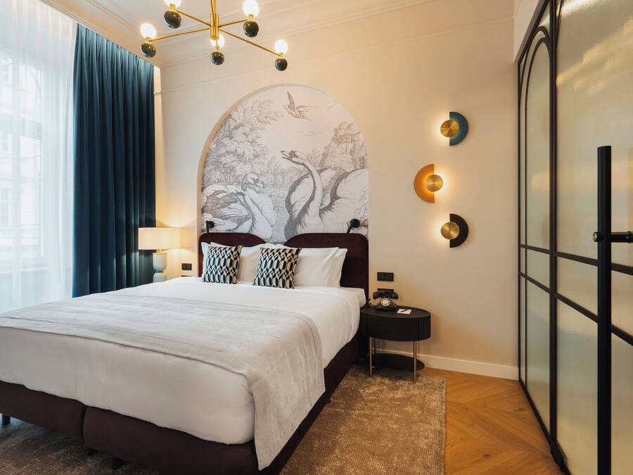 Habitación de hotel con una cama grande, una mesita de noche, una lámpara de pared y un adorno mural.
