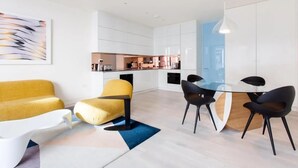 A modern living room with a yellow sofa, a glass dining table with black chairs, and a kitchen in the background. - Central London Charm One Bedroom Apartment (London)