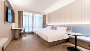A modern hotel room with a large bed, a small table, a sofa, and a TV mounted on the wall.