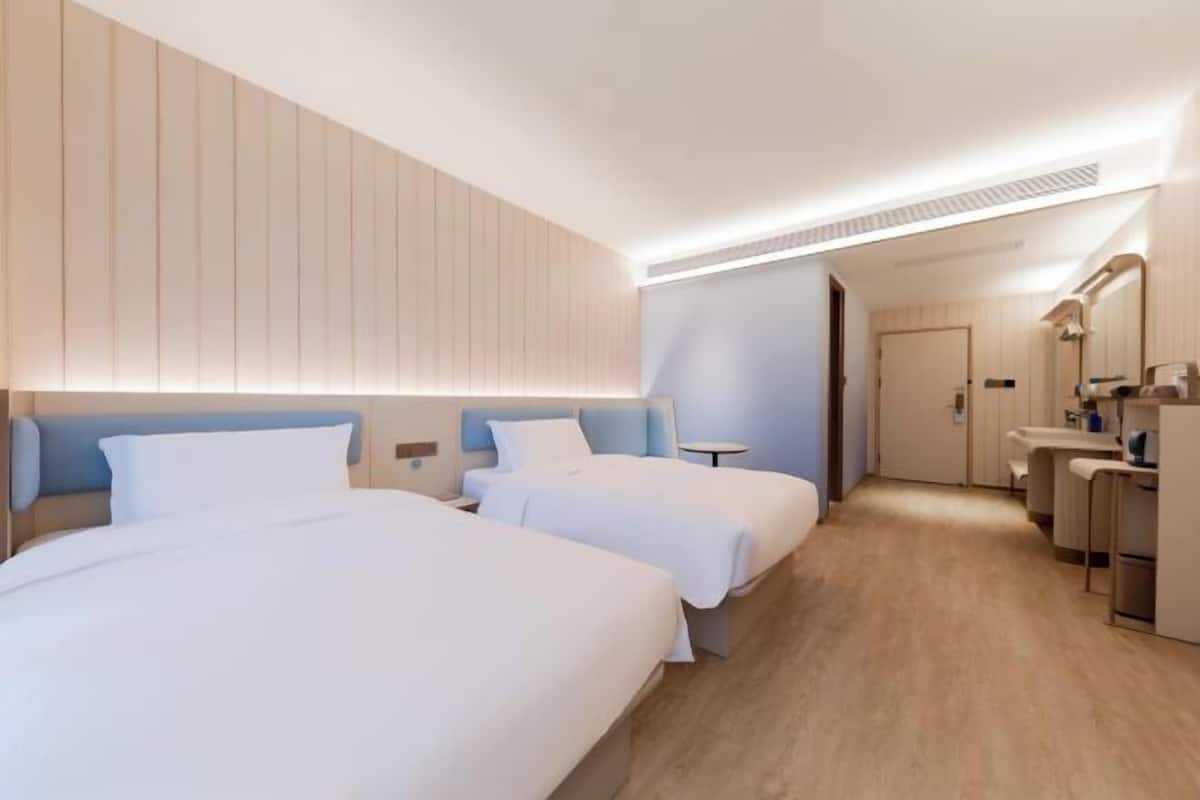 Une chambre d’hôtel avec deux lits, une petite table, un miroir et une kitchenette.