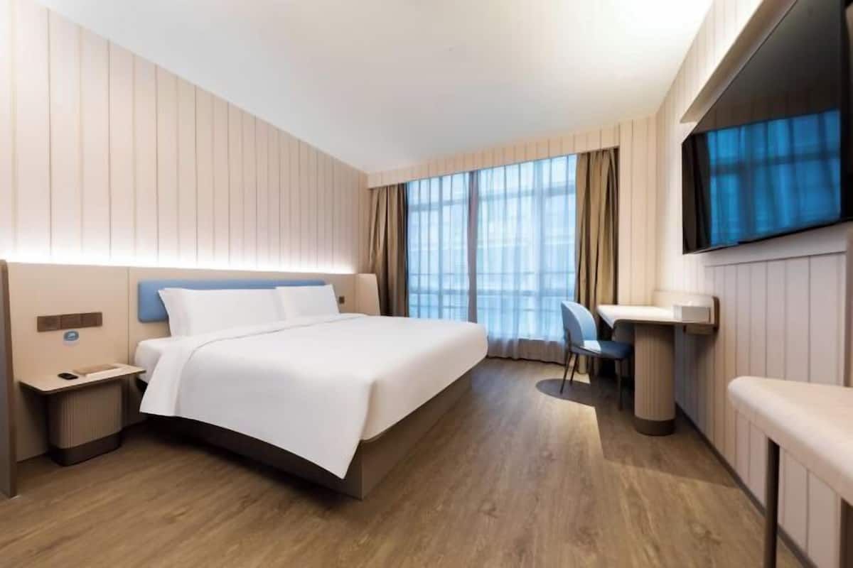 Une chambre d’hôtel moderne, dotée d’un grand lit, d’un bureau et d’un téléviseur fixé au mur.