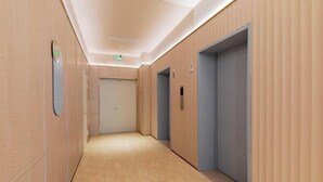 A modern hotel corridor with wooden paneling, a light-colored floor, and two elevators.