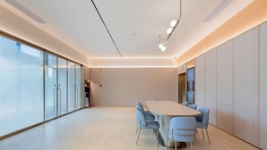 A modern conference room with a long table, blue chairs, and a large window providing natural light.