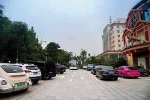 A street with parked cars and a bus, buildings with signage, and trees. - Quzhou Ying Hotel (Quzhou)