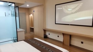 A modern hotel room with a bed, a large mirror, a flat-screen TV, and a wooden bench. - Quzhou Ying Hotel (Quzhou)