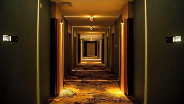 A hotel hallway with a carpeted floor, a light fixture at the end, and a door at the far end. - Quzhou Ying Hotel (Quzhou)