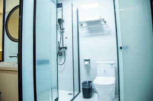 Un baño moderno con cabina de ducha de vidrio, inodoro y un cubo de basura.