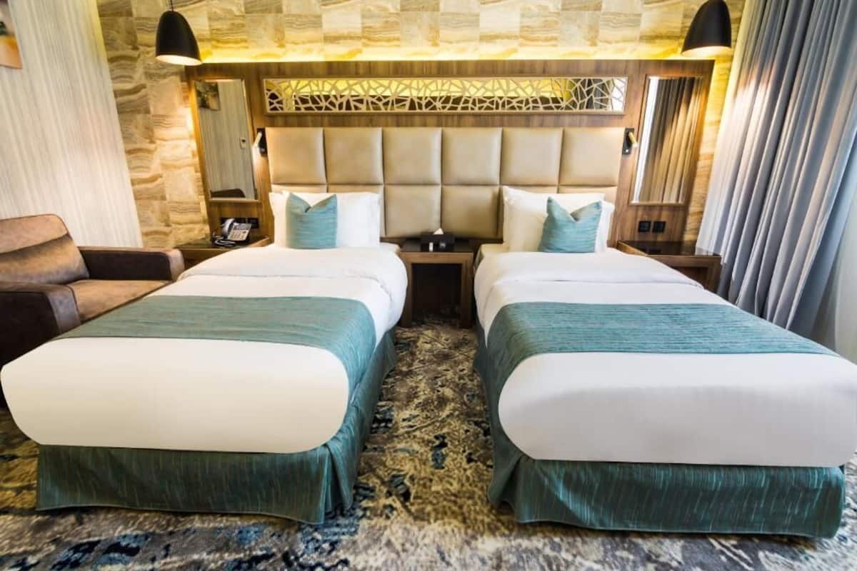 Ein Hotelzimmer mit zwei Betten, einem Schlafsofa, einem Kopfteil mit geometrischem Muster und einem gemusterten Teppich.