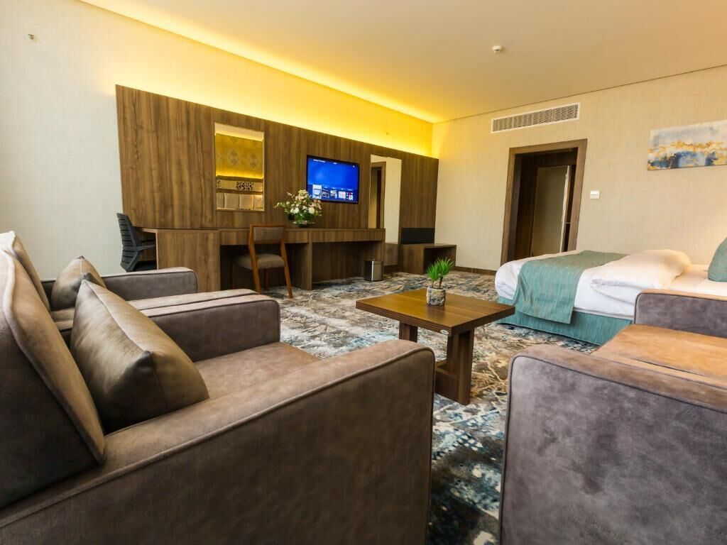 A hotel room with a sofa, a bed, a TV, and a small table with a plant.