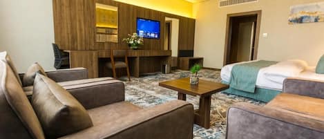 A hotel room with a sofa, a bed, a TV, and a small table with a plant.