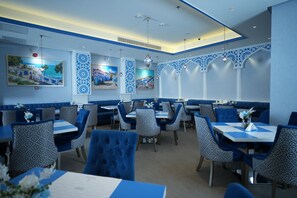 Un restaurante con decoración azul y blanca, con sillas y mesas con diseños, y obras de arte en las paredes.