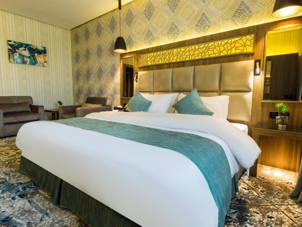 Ett modernt hotellrum med en stor säng, en soffa, ett skrivbord och en dekorativ väggpanel.