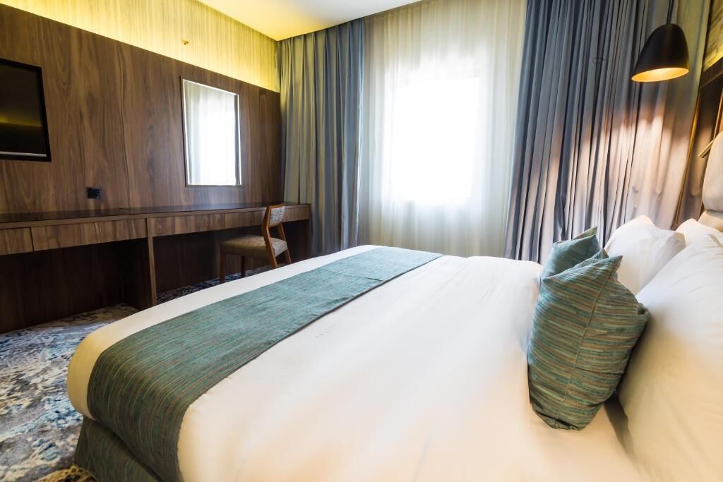 A hotel room with a large bed, a desk, a chair, and a TV mounted on the wall.