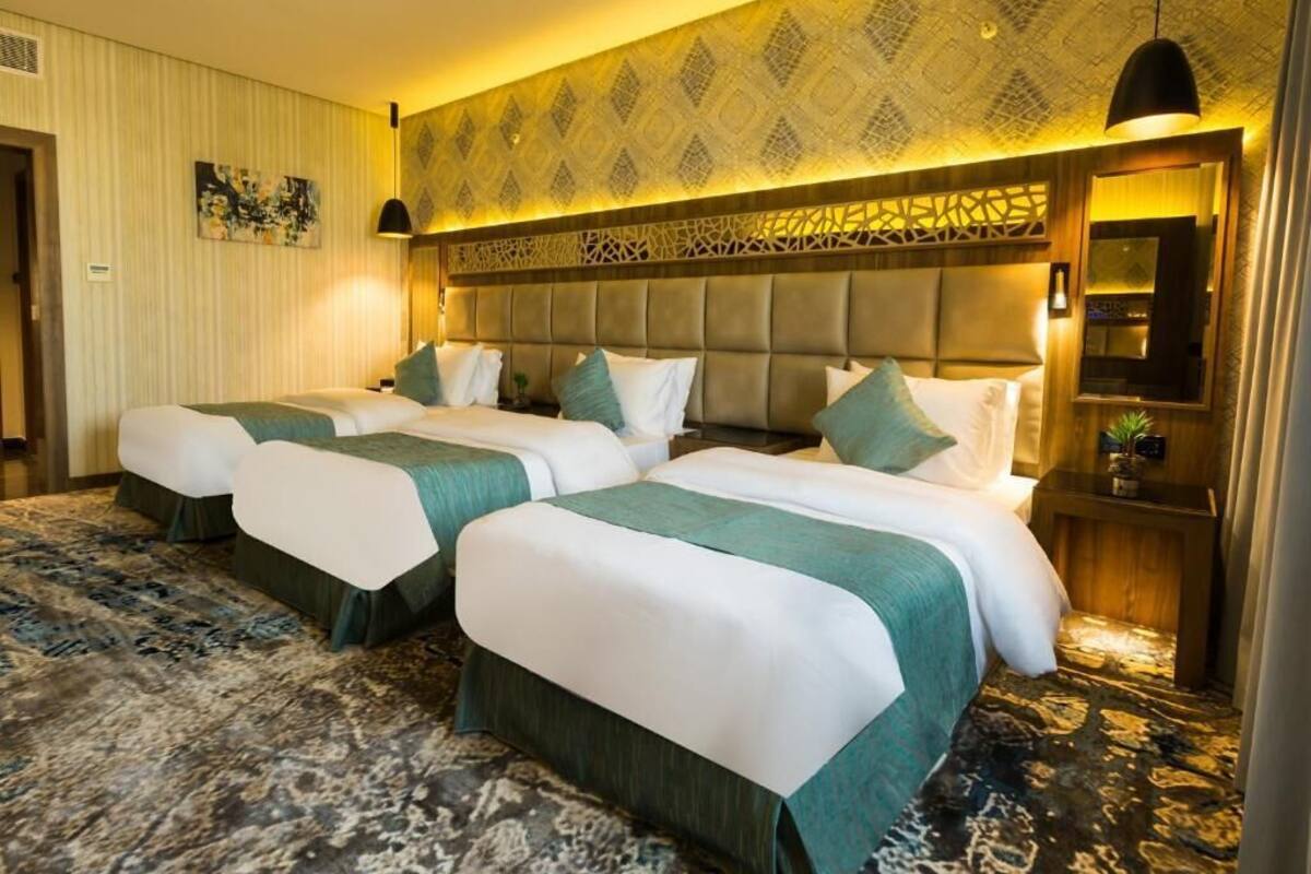 Ein Hotelzimmer mit zwei Betten, einem großen Kopfteil, einer Wand mit Muster und einem kleinen Tisch mit Pflanze.