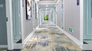 A hotel hallway with framed artwork on the walls, a patterned carpet, and a green exit sign. - Junfu Hotel (Guangzhou Panyu Square Metro Station) (Guangzhou)