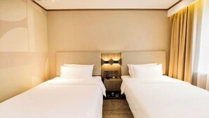 Een hotelkamer met twee enkele bedden, een nachtkastje met een lamp, en uitzicht op de straat door het raam.