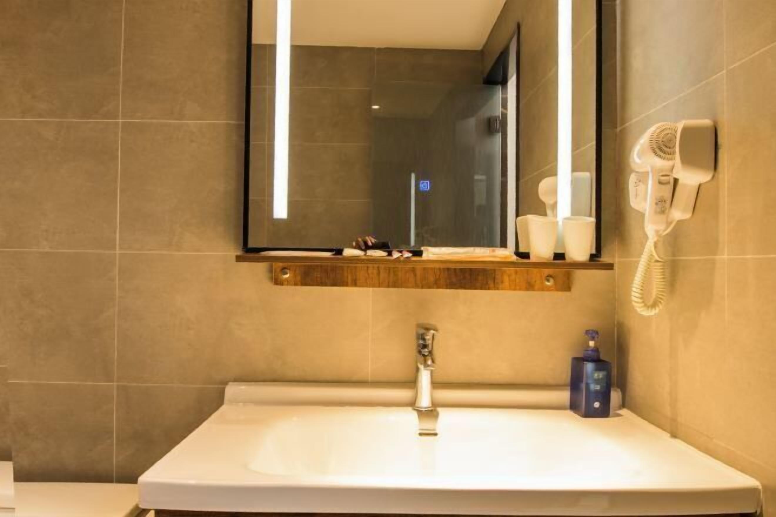 A bathroom with a large mirror, a sink, a hairdryer, and a towel rack.