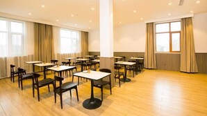 Een ruime vergaderzaal met meerdere tafels en stoelen, grote ramen met gordijnen, en een whiteboard aan de muur.