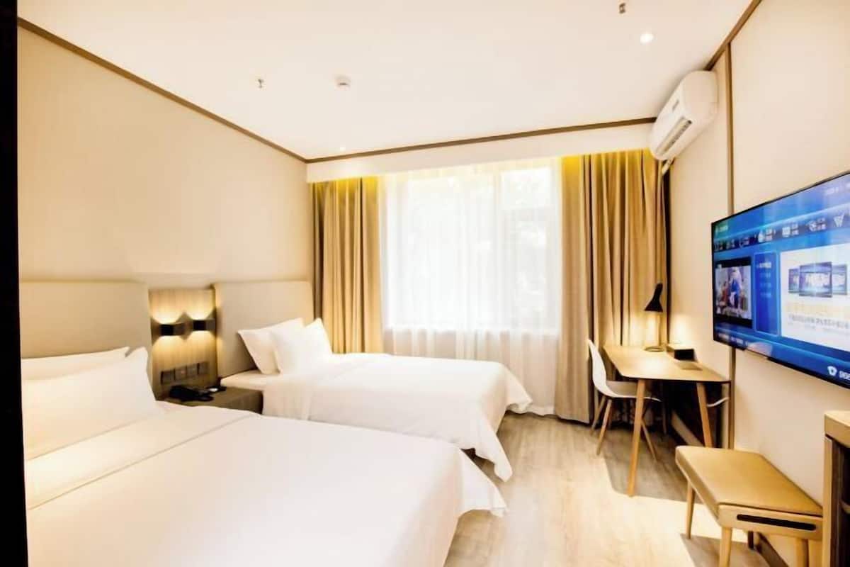 A hotel room with two beds, a desk, a chair, a TV, and a window with curtains.