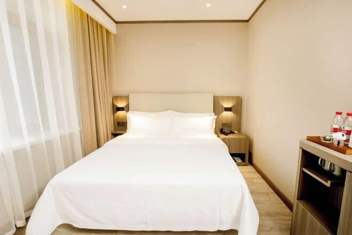 A hotel room with a large bed, bedside lamps, a nightstand, and a minibar.