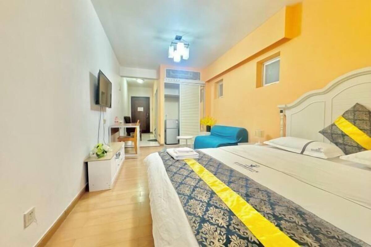 Ein Hotelzimmer mit Bett, Schreibtisch, Stuhl, Fernseher und einem im Hintergrund sichtbaren Badezimmer.