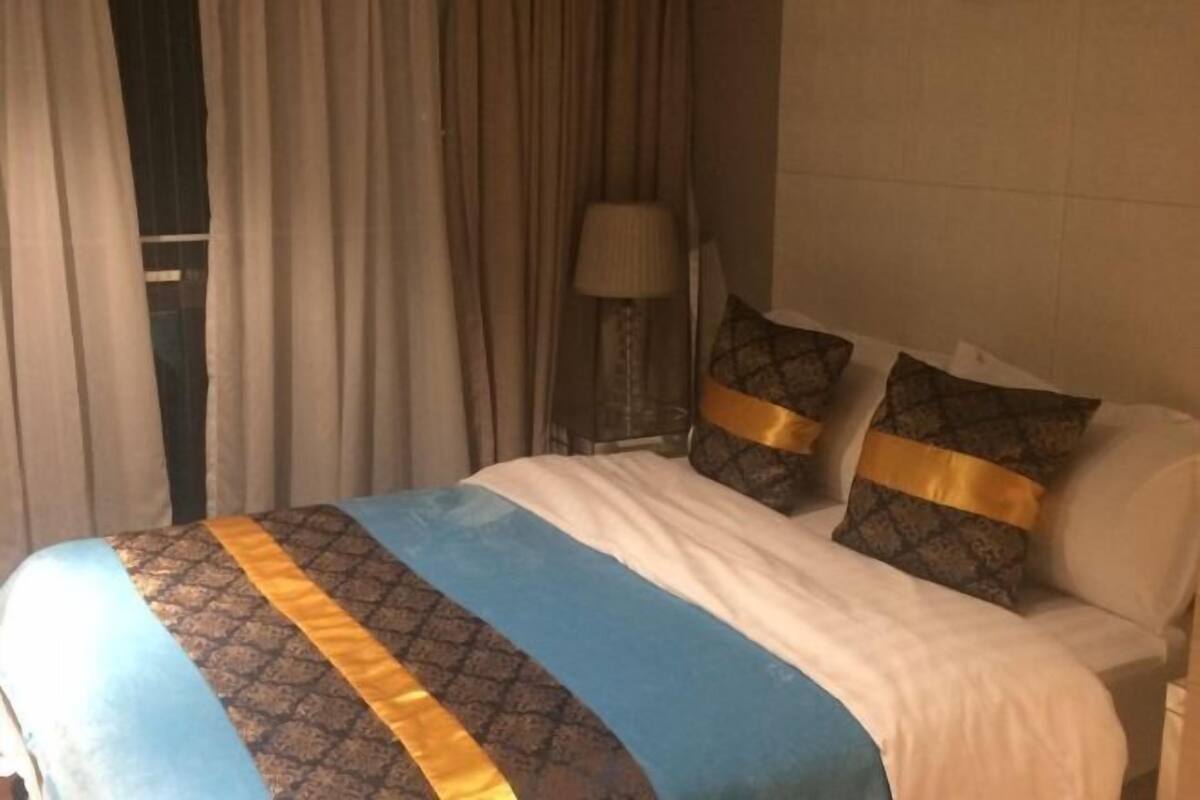 Ein Hotelzimmer mit Bett, Vorhängen, einer Lampe und gemusterten Kissen.