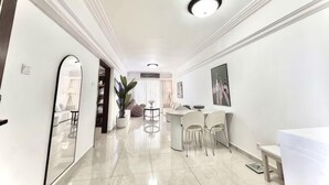 Ein moderner Hotelkorridor mit heller Einrichtung, einem runden Esstisch mit Stühlen und einem großen Spiegel an der linken Wand.