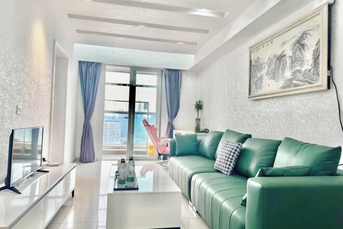 Ein modernes Wohnzimmer mit einem grünen Sofa, einem Flachbildfernseher und einem großen Fenster mit Vorhängen.