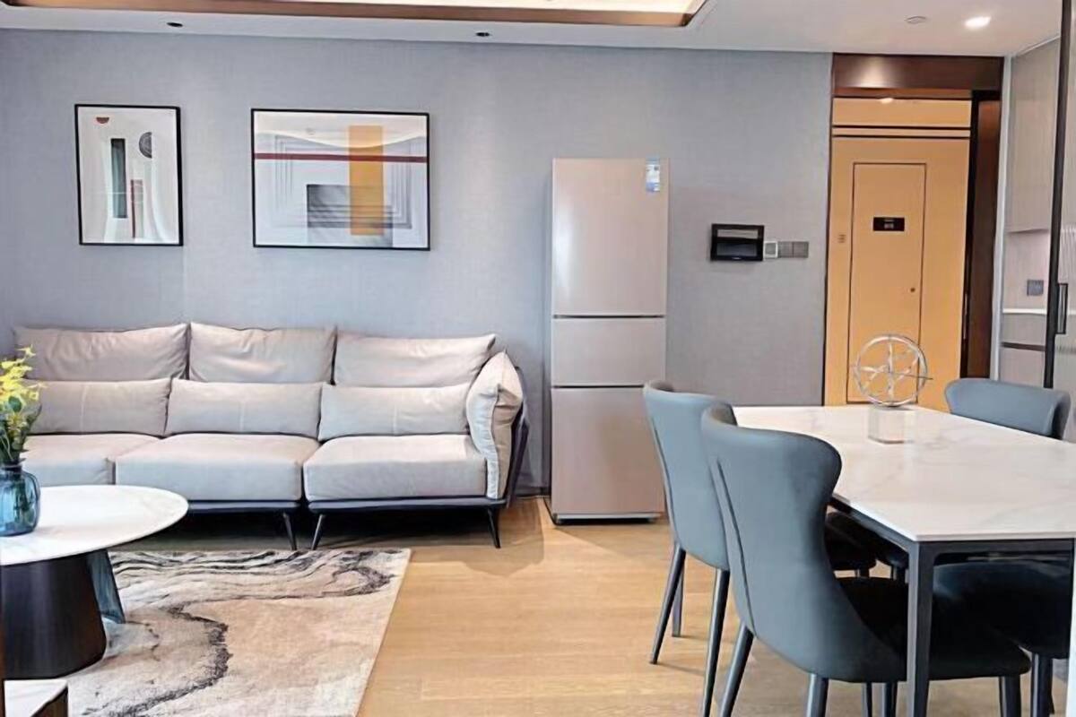 Ein modernes Wohnzimmer mit einer Couch, einem Esstisch mit Stühlen, einem Kühlschrank und abstrakter Wandkunst.