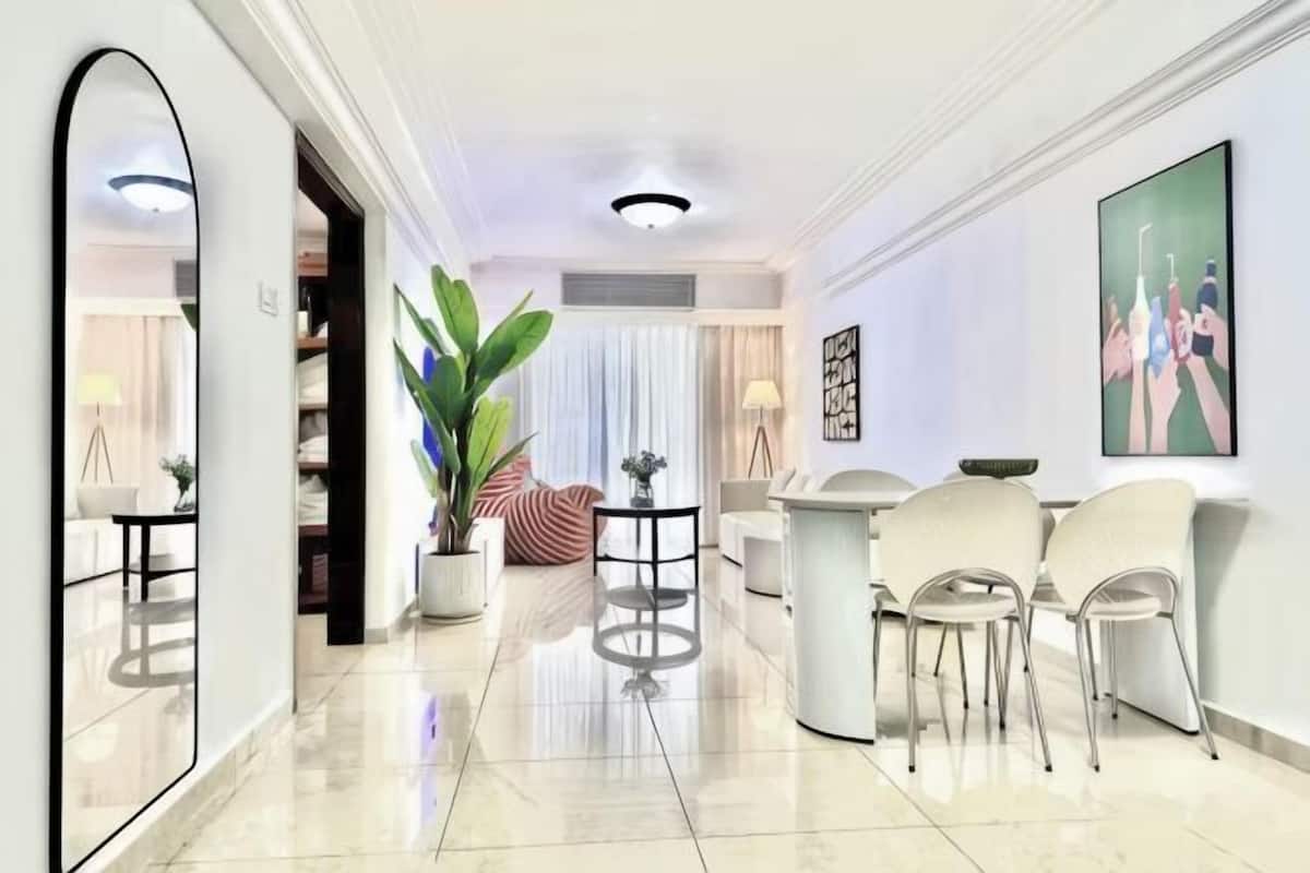 A modern hotel lobby with a large mirror, a reception desk, seating area, and a large plant.