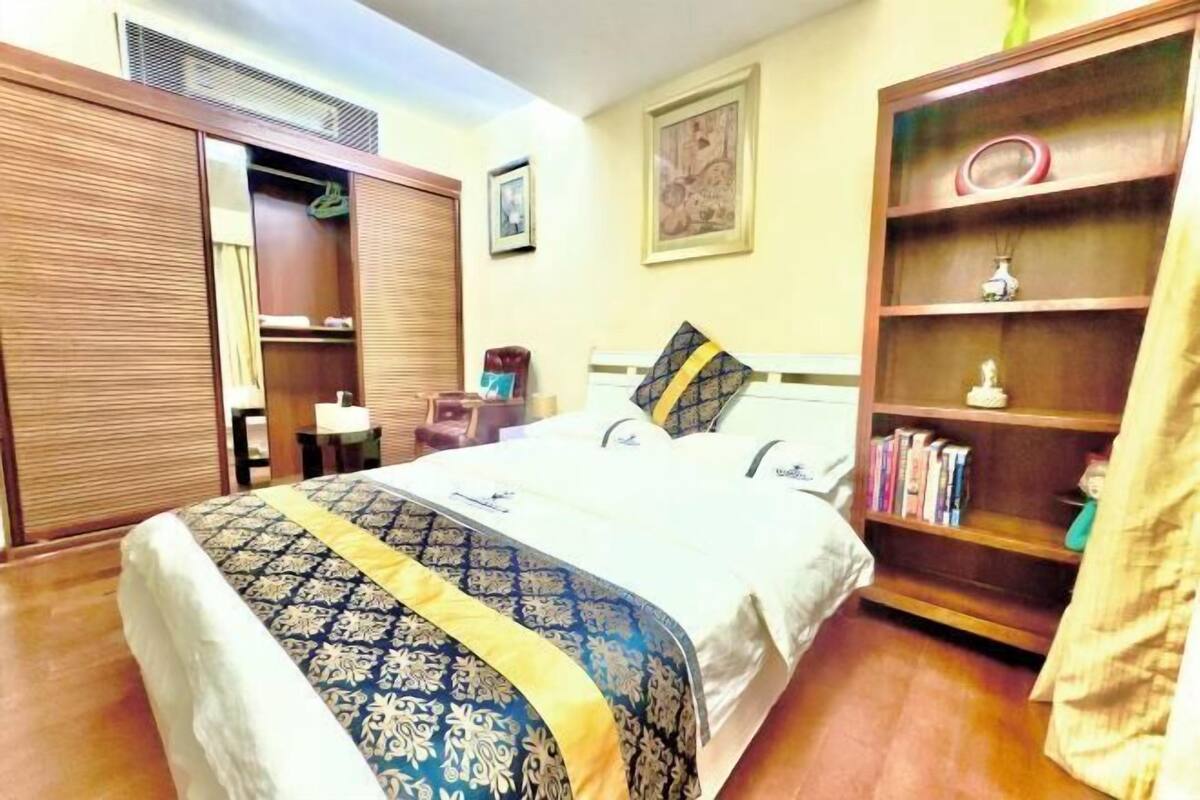 Ein Hotelzimmer mit Bett, Schrank, Nachttisch, Stuhl, Bücherregal und einem Wandbild.