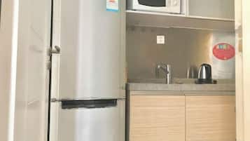 A compact kitchen with a stainless steel refrigerator, a microwave, a sink, and wooden cabinets.
