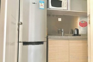 Una cocina compacta con un refrigerador de acero inoxidable, un microondas, un lavamanos y armarios de madera.