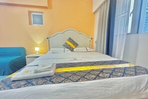 Una habitación de hotel con cama, mesita de noche, ventana con cortinas y un pequeño ventanal sobre la cama.