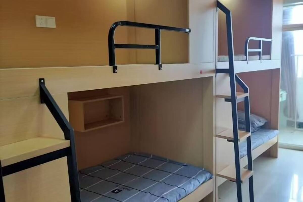 Habitación con literas, una pared de madera, un estante pequeño y una ventana.