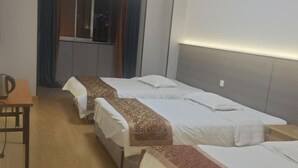 A hotel room with three single beds, a wooden table, and a window with curtains.