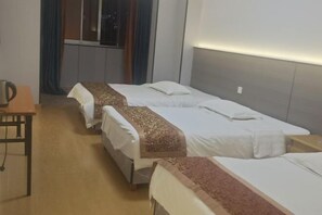 Une chambre d’hôtel avec trois lits simples, une table en bois et une fenêtre avec des rideaux.
