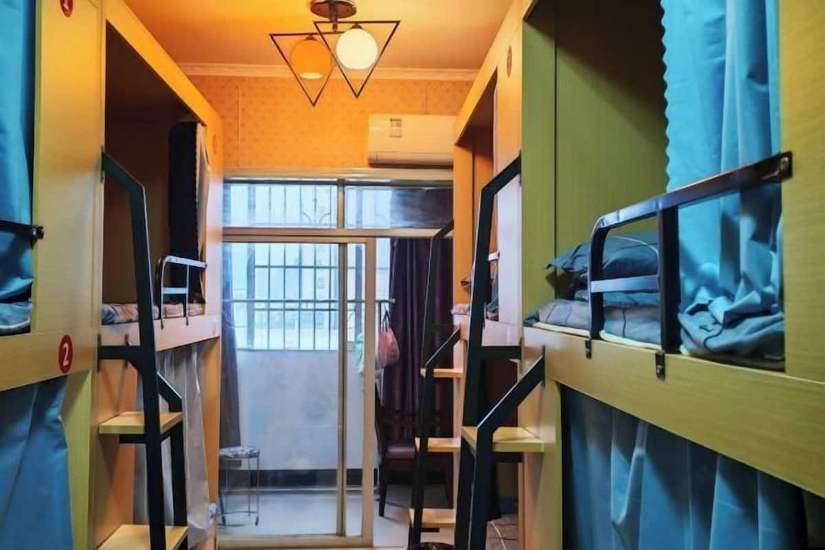 Un dormitorio con literas, una escalera, una puerta que da a un espacio exterior y una lámpara colgante.