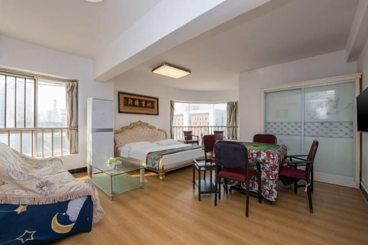 Una habitación de hotel con una cama, una mesa de comedor con sillas, un televisor y ventanas grandes.