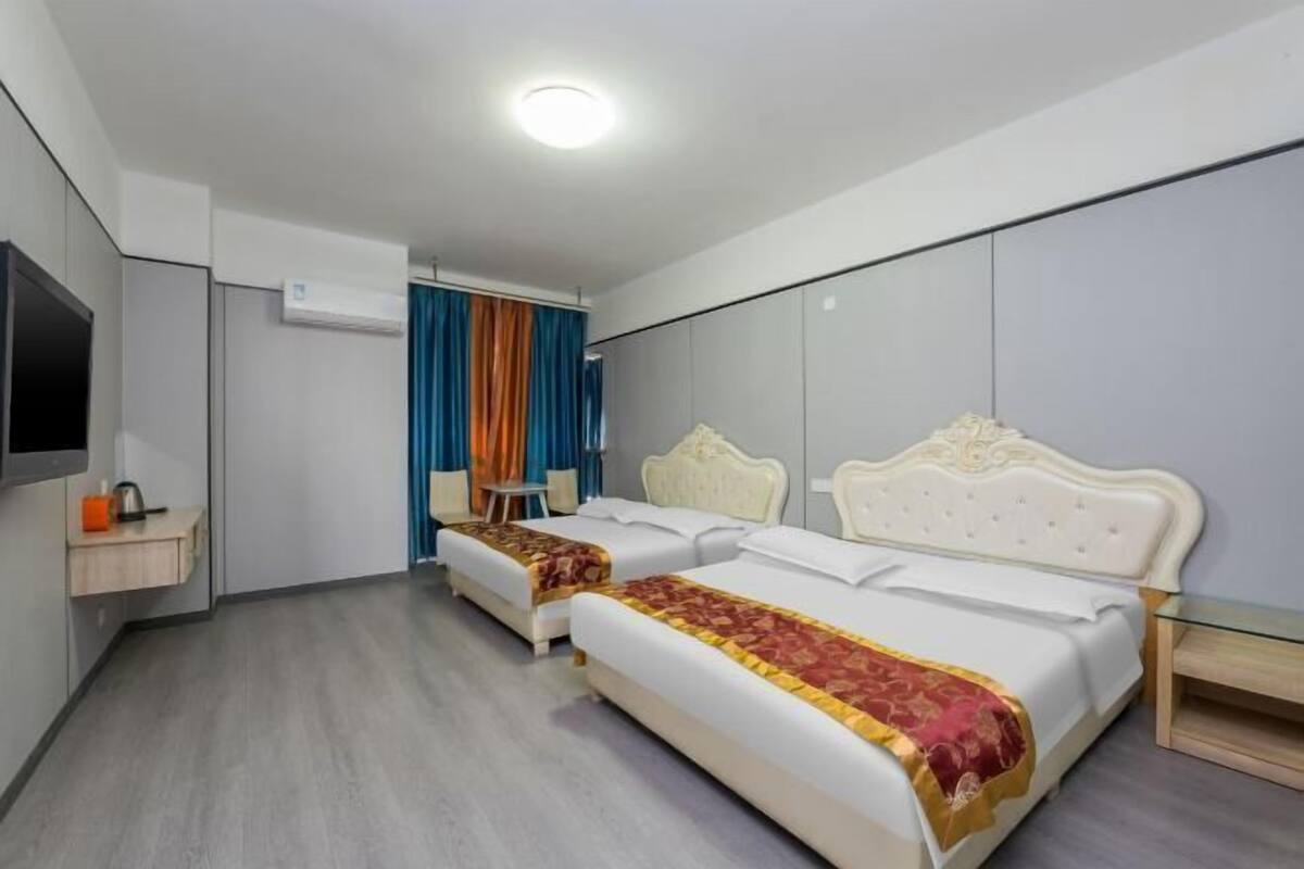 Una habitación de hotel con dos camas, un televisor, una mesita y un espejo.