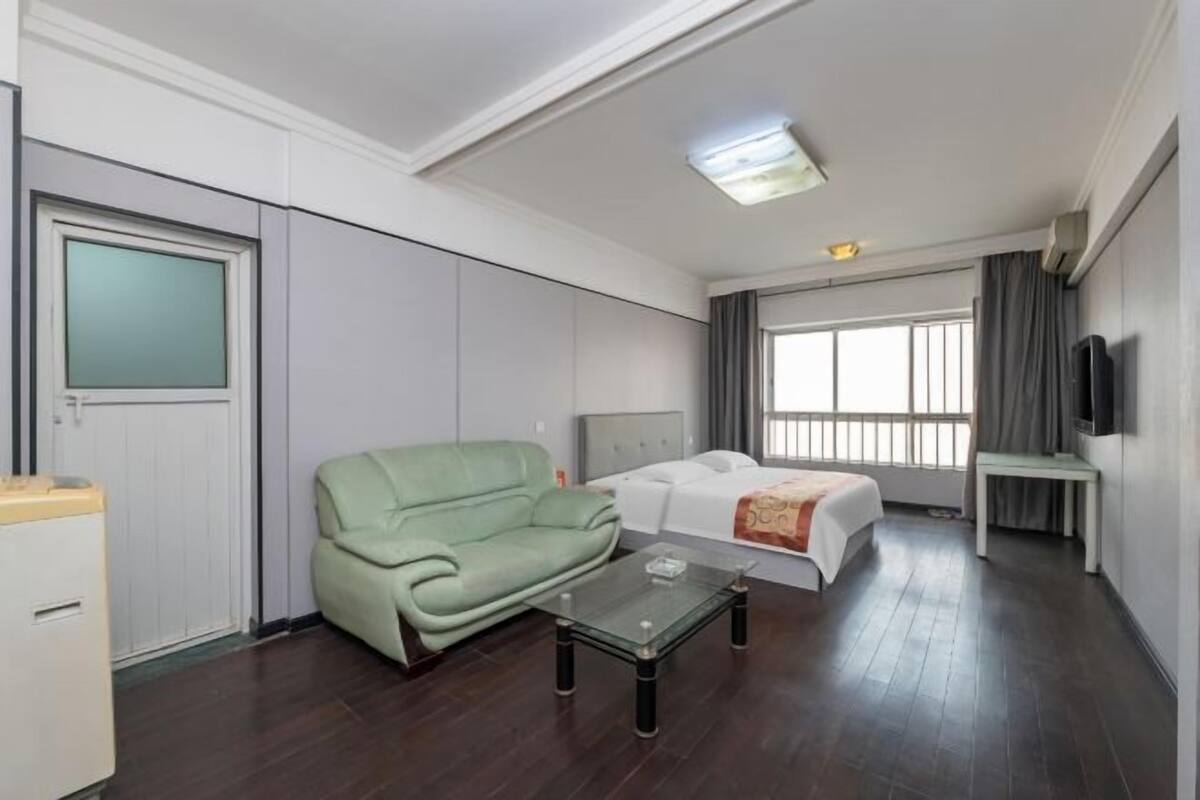 Habitación de hotel con sofá, cama, una mesita, televisor y ventana con cortinas.